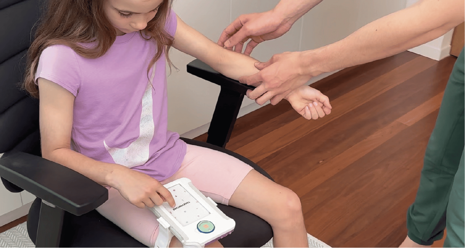 Child sitting in a chair with the Tokeventure module on their lap with a medical professional touching their arm. This is in preparation for a blood test. 